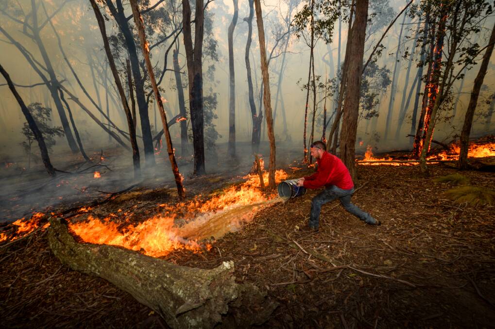 Ross Upfield douses flames near the house with water. Picture: Justin McManus
