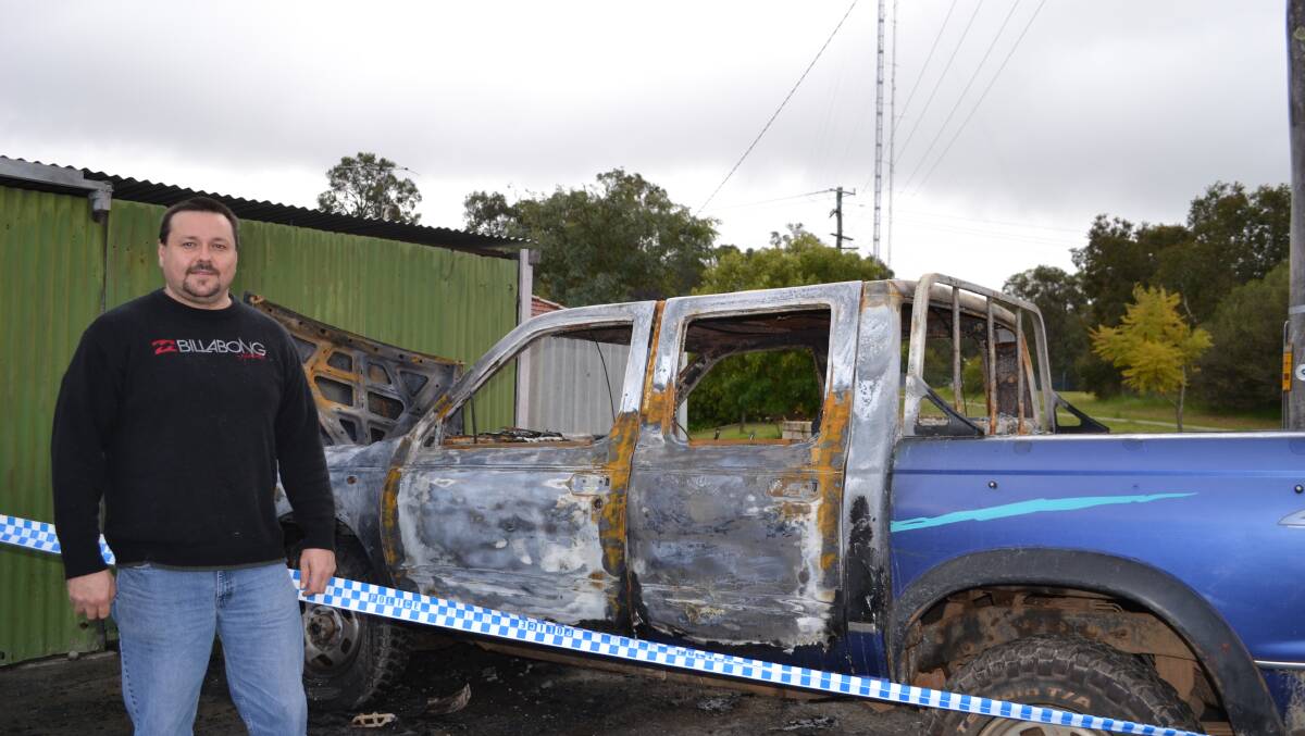 Dean Goltz stands in front of his burnt out car which was deliberately set on fire over the weekend by vandals